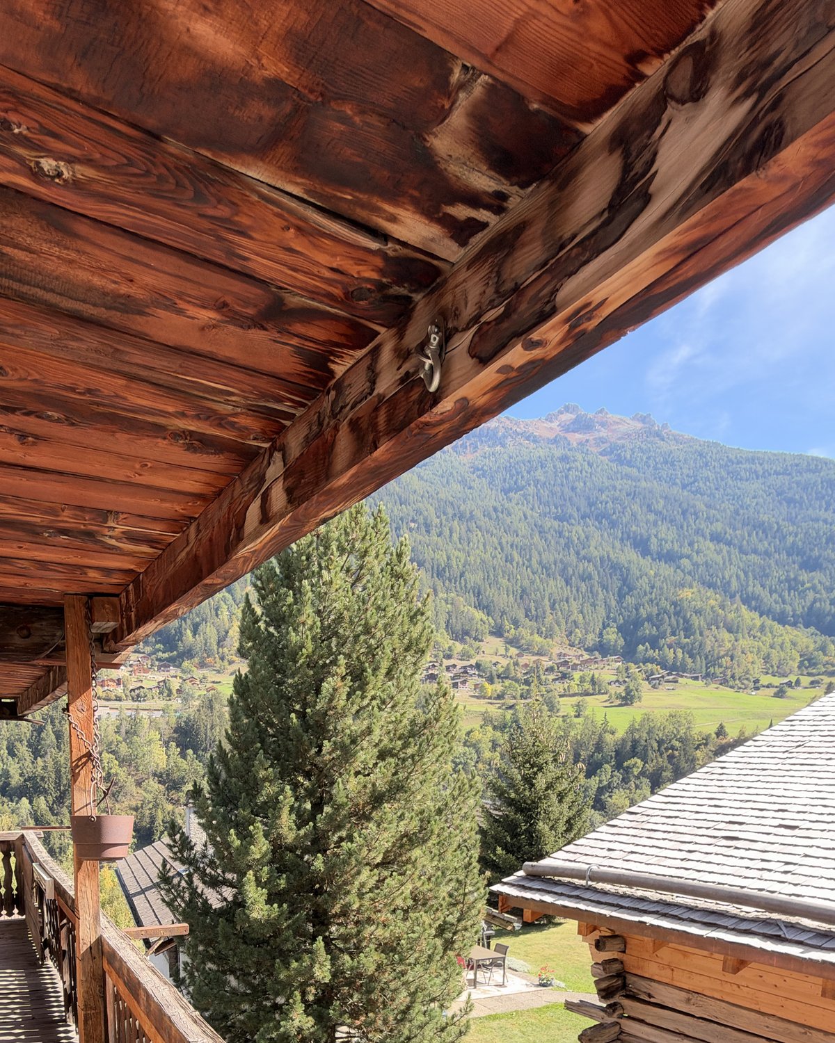 Balcon en bois ouvert sur un village et les montagnes du Valais, photographie illustrative